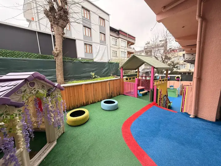 Oyun evi, boyalı lastikler ve yeşil-mavi zeminiyle okul bahçesi